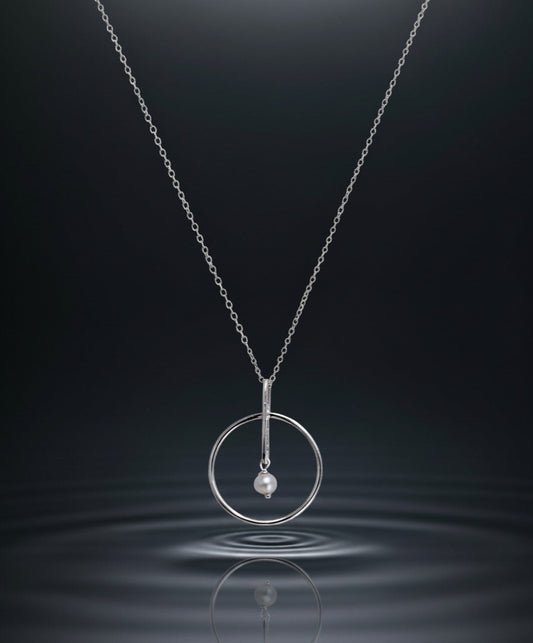 Silver necklace with a circular pendant and pearl on a dark water background