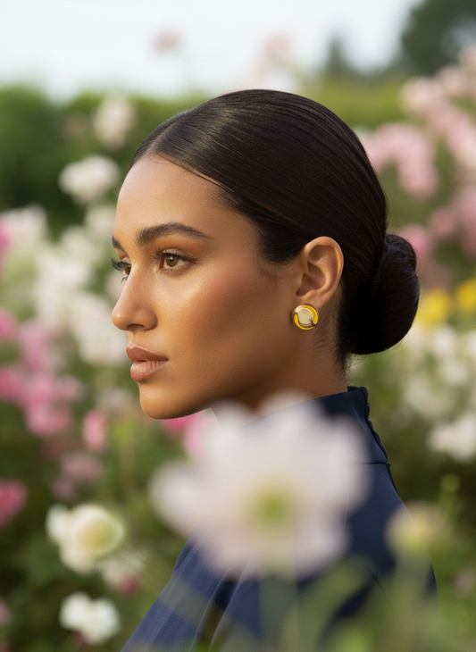 Woman with a bun and yellow earrings standing in a garden with flowers