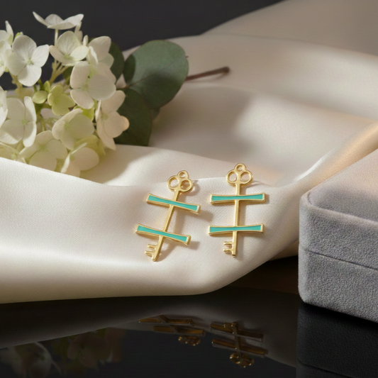Gold and green earrings on a white surface with flowers and a jewelry box.
