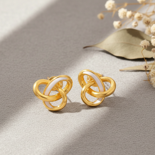 Gold and white earrings on a textured surface with dried flowers.