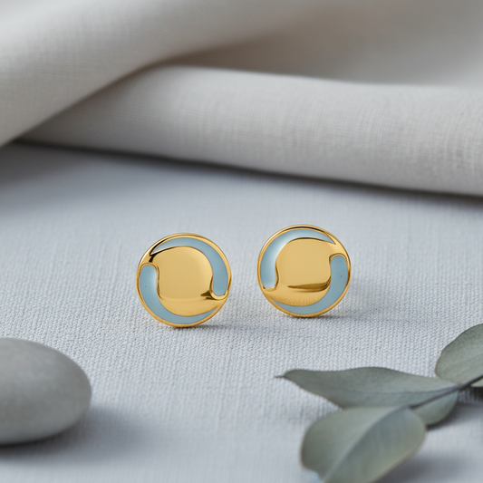 Gold and light blue circular earrings on a neutral background with leaves.
