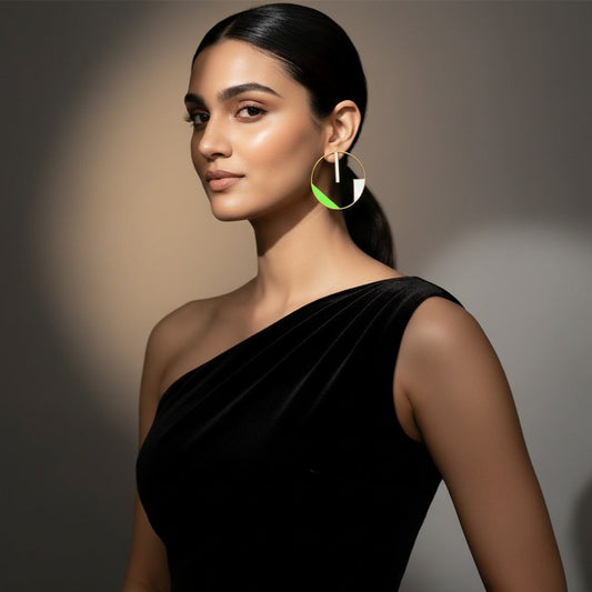 Woman wearing a black one-shoulder dress with large hoop earrings on a neutral background