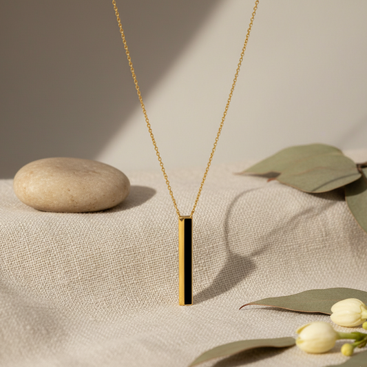 Gold necklace with a black pendant on a textured surface with leaves and flowers.