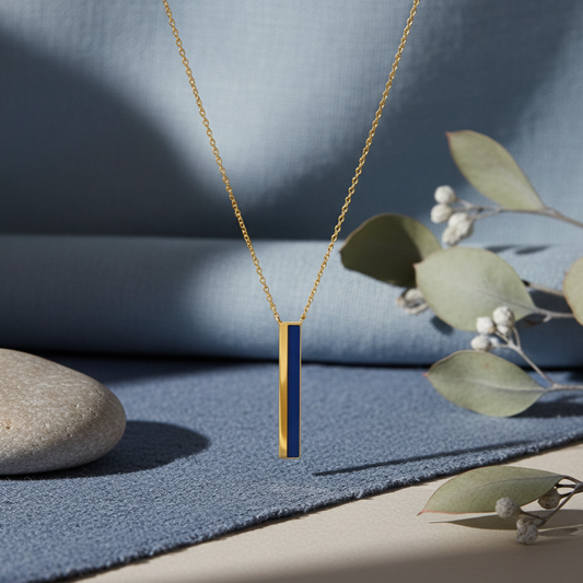 Gold necklace with a blue pendant on a textured surface with leaves and a stone.