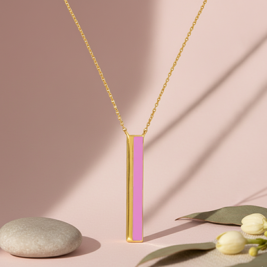 Gold necklace with a pink pendant on a pink background with leaves and a stone.