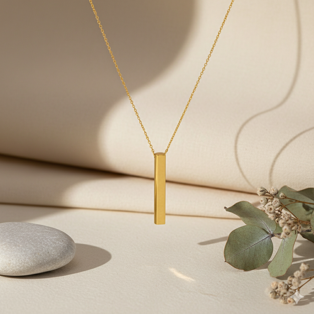 Gold necklace with a vertical bar pendant on a neutral background with a stone and leaves.