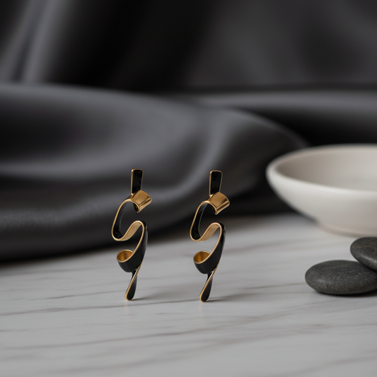 Pair of black and gold earrings on a gray surface with a dark fabric background