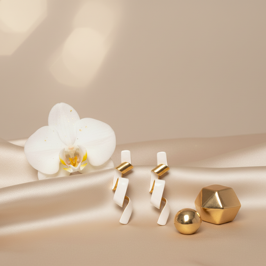 Gold and white geometric earrings on a beige surface with a white orchid.