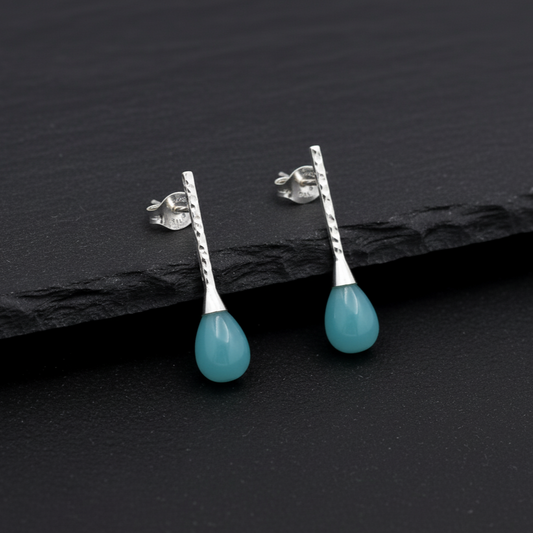 Teardrop-shaped turquoise earrings with silver posts on a dark slate background