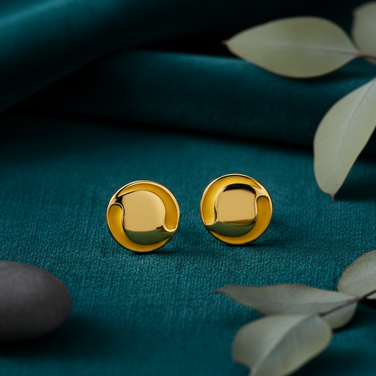 Gold earrings on a teal fabric background with leaves.