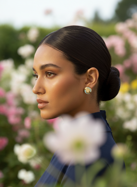 Woman with a bun and earrings standing in a garden with flowers