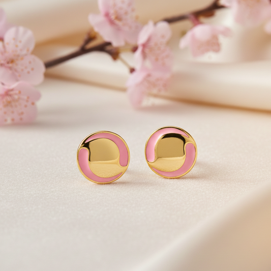 Gold and pink earrings on a light surface with pink flowers in the background