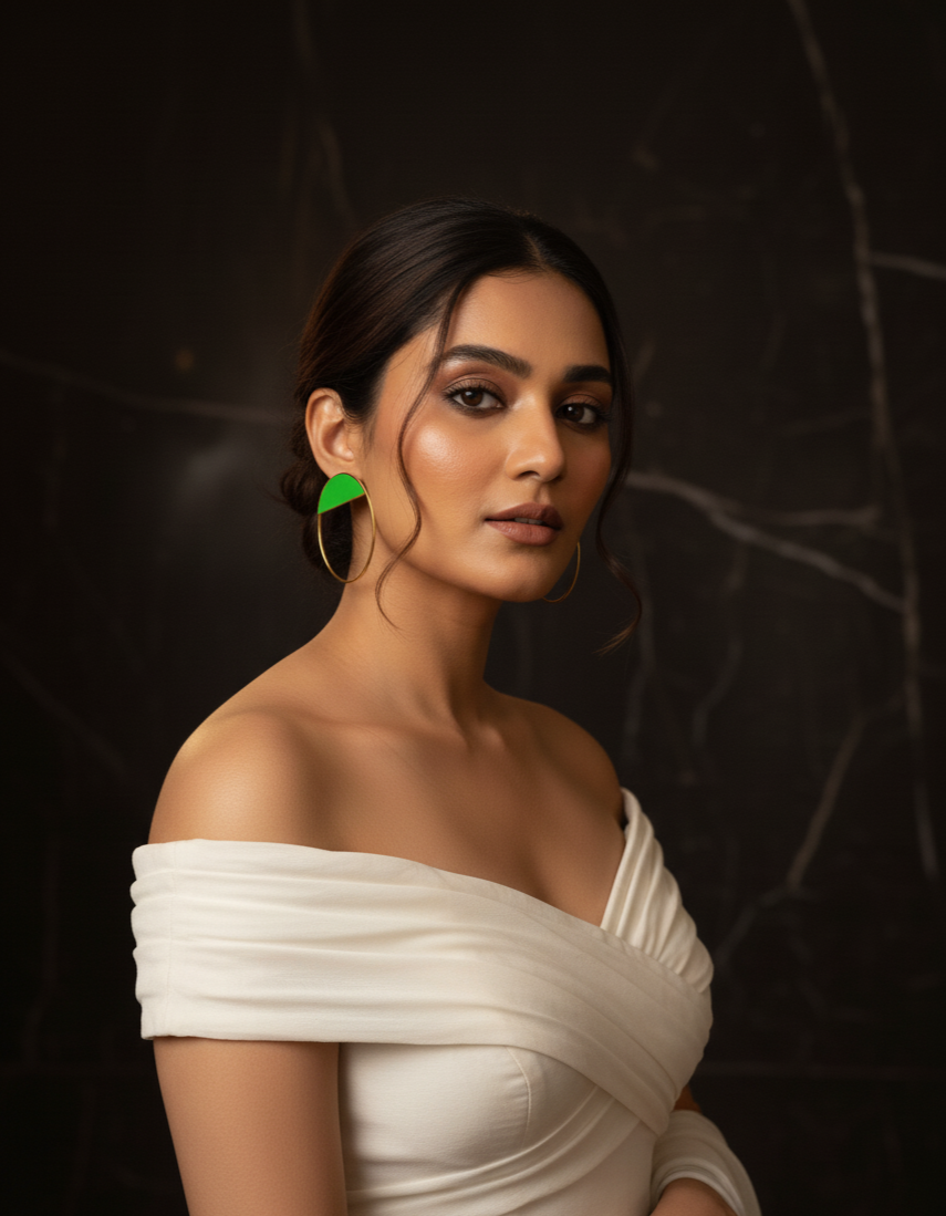 Woman wearing a white off-shoulder top against a dark background wearing green hoops.